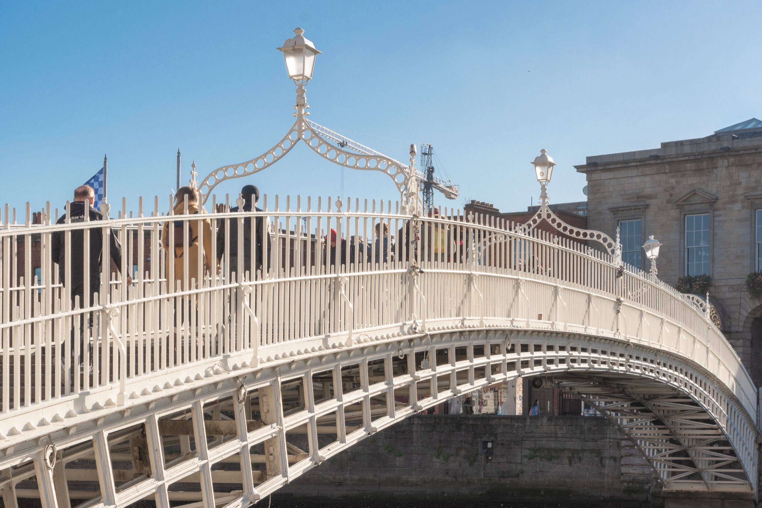 Die weiß lackierte gusseiserne Ha'penny Bridge über den Liffey mit Fußgängern unter strahlend blauem Himmel.