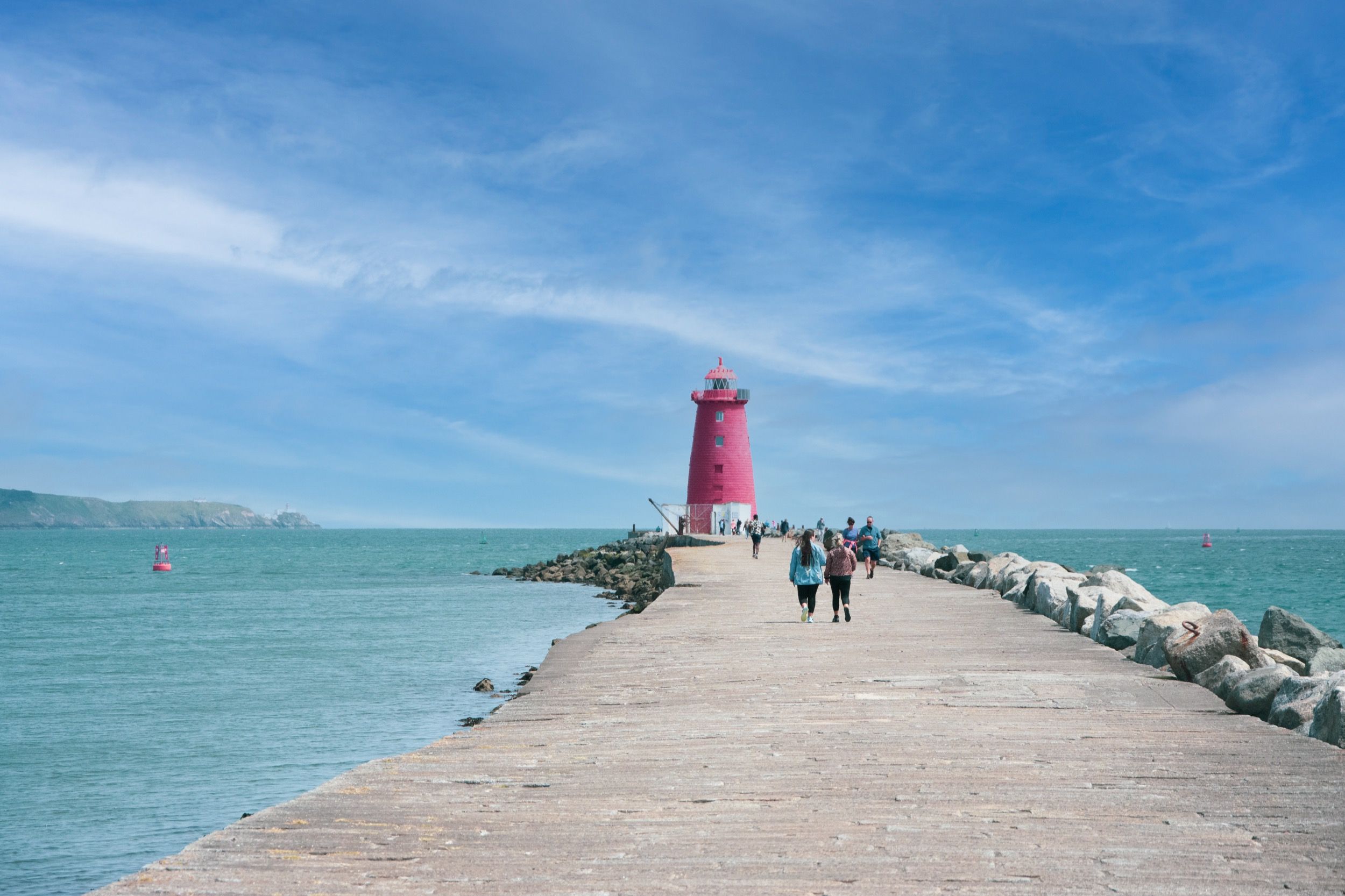 Roter Leuchtturm auf Mole in Howth mit Klippen und Touristen auf der Pier.