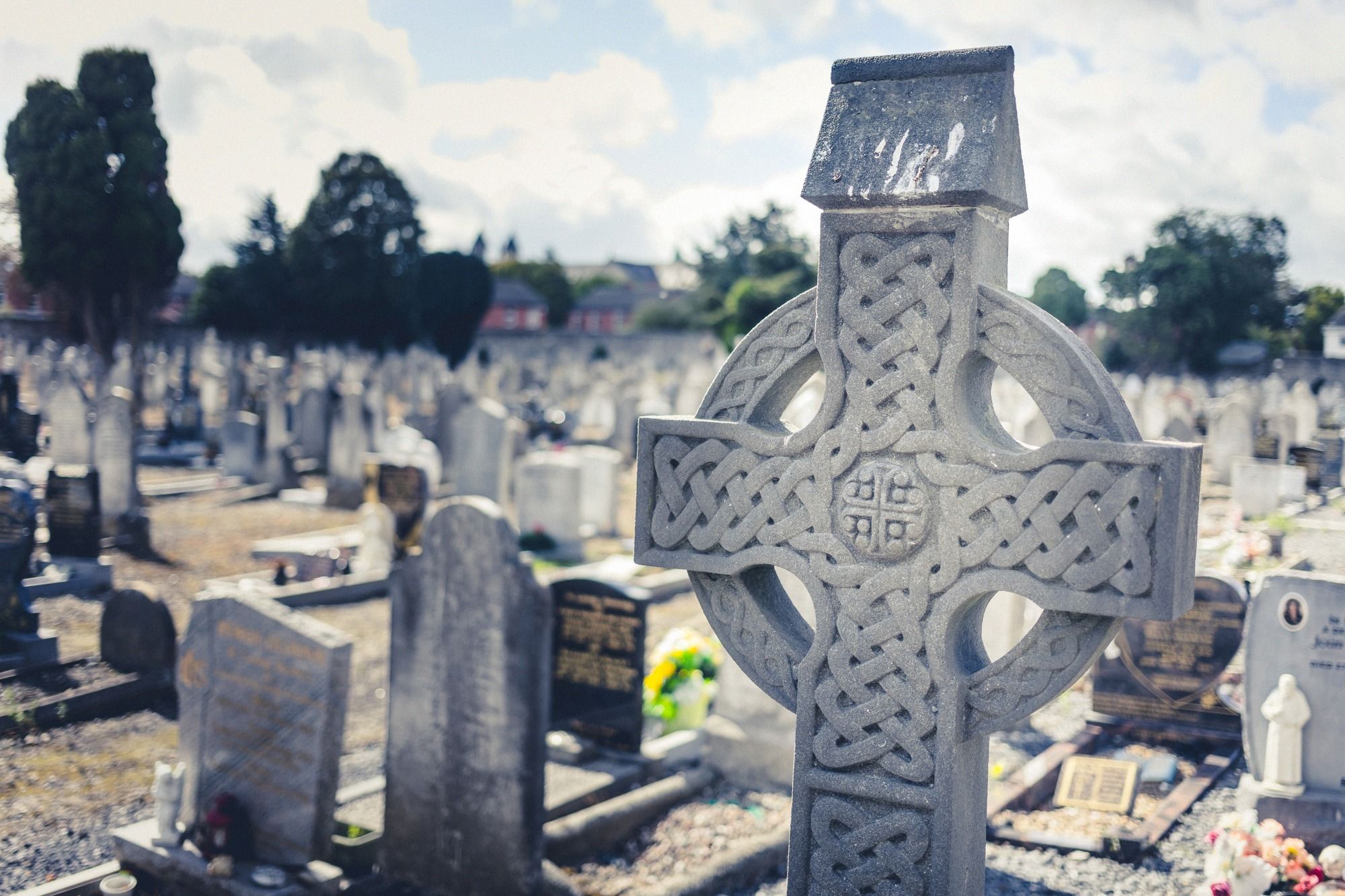 Friedhof mit charakteristischem keltischem Kreuz und weiteren Grabmalen im Hintergrund.