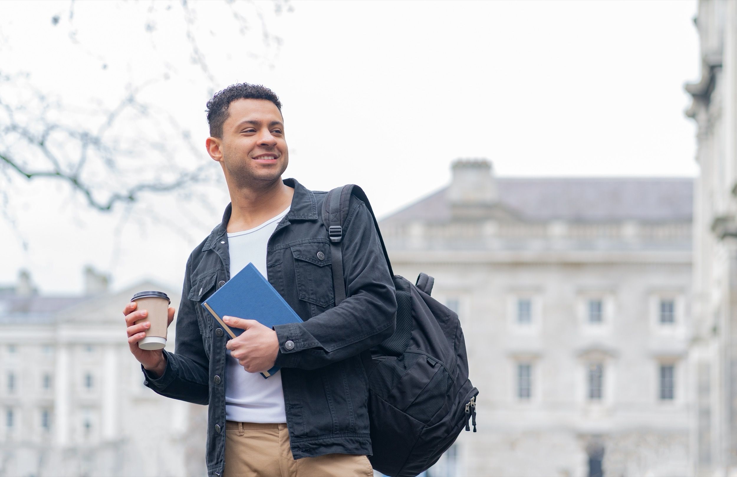 Junger Student mit Kaffee und Buch vor georgianischem Backsteingebäude, symbolisiert Studentenleben und internationale Bildung in Dublin.
