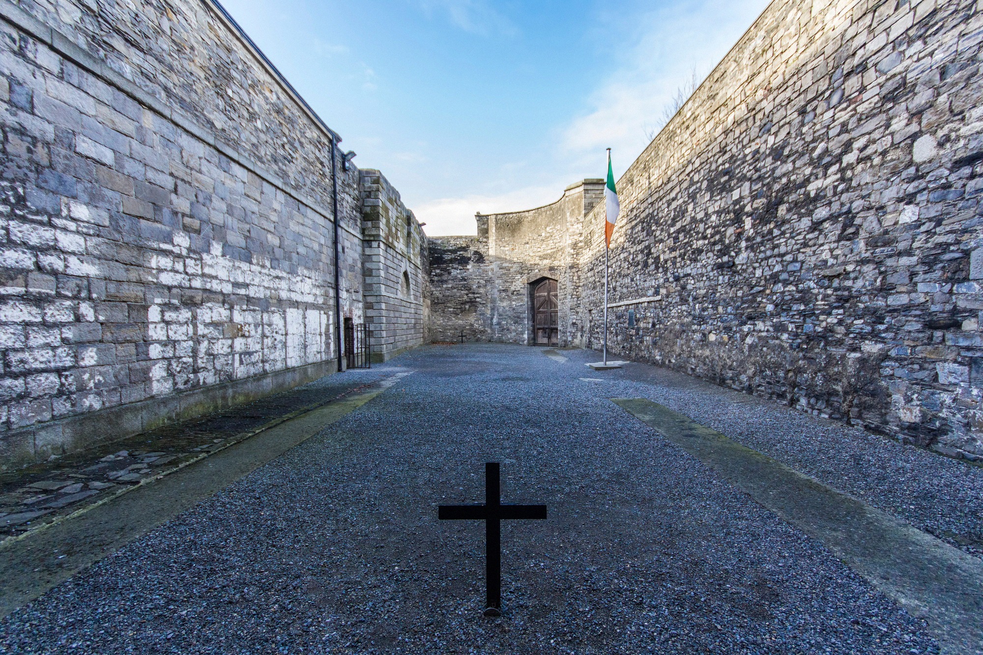 Der Hinrichtungshof von Kilmainham Gaol mit dem markanten schwarzen Kreuz auf dem Kieselboden und der irischen Trikolore, Gedenkstätte für die Führer des Osteraufstands 1916.